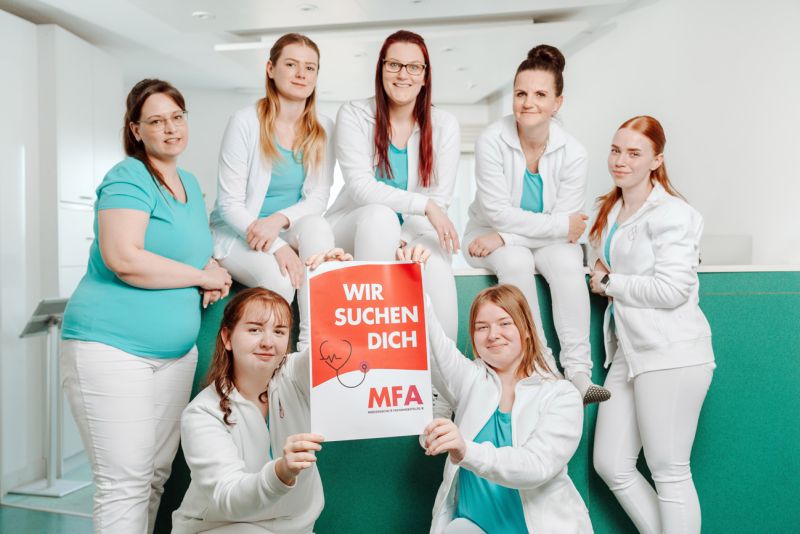 Team der Herzpraxis Magdeburg mit einem Plakat „Wir suchen dich – MFA“ für neue medizinische Fachangestellte.